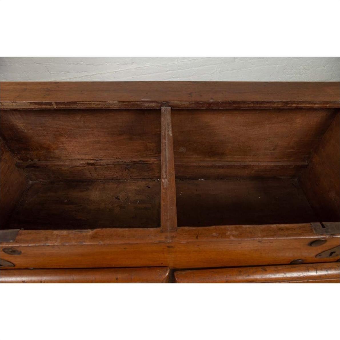 Brown teak wood blanket chest with iron nailheads on wheels, open to show two compartments.