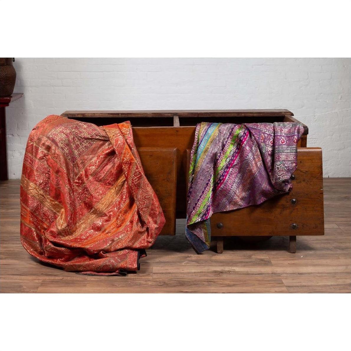 Red and purple fabrics on antique Javanese teak wood chest with iron nailheads, styled indoors.