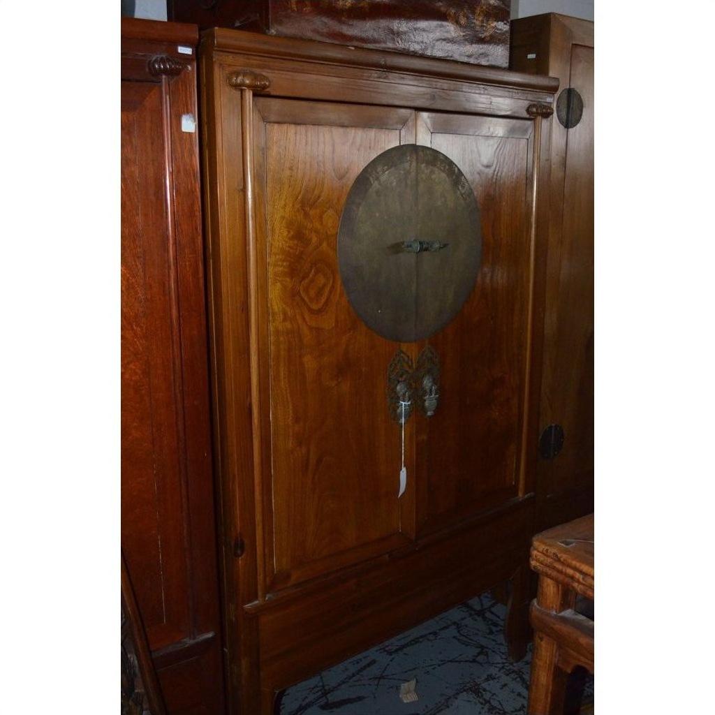Wood armoire in neutral finish with double doors, round medallion hardware, and central decorative lock.