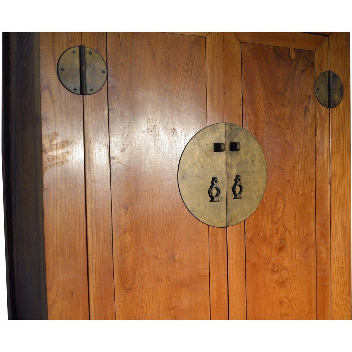 Close-up of brown wooden armoire doors with round brass handles and metal accents.