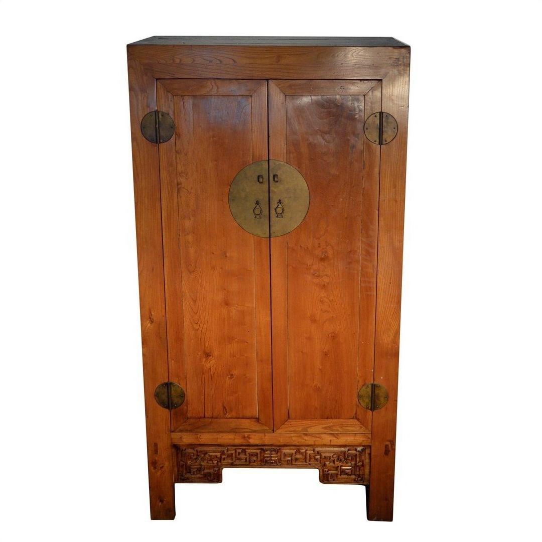 Brown wooden antique Chinese armoire with double doors, brass handles, and carved base panel.