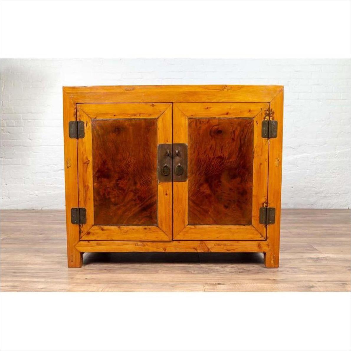 Two-toned burl and elm wood Chinese antique cabinet with doors against a white brick wall indoors.
