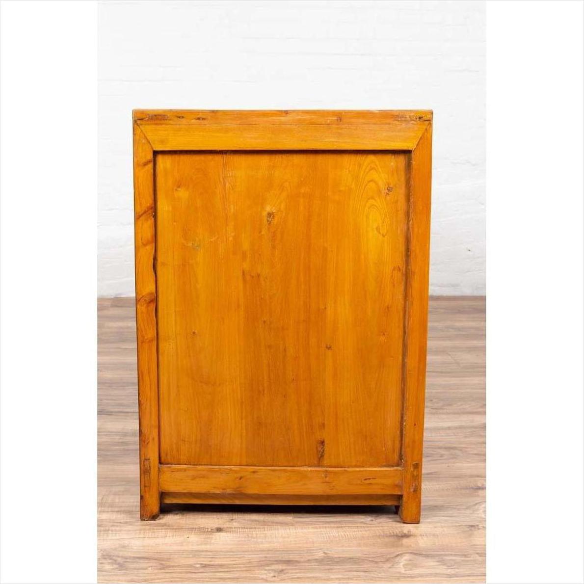 Two-toned burl and elm wood antique cabinet with doors, positioned against a light brick wall and wood floor indoors.