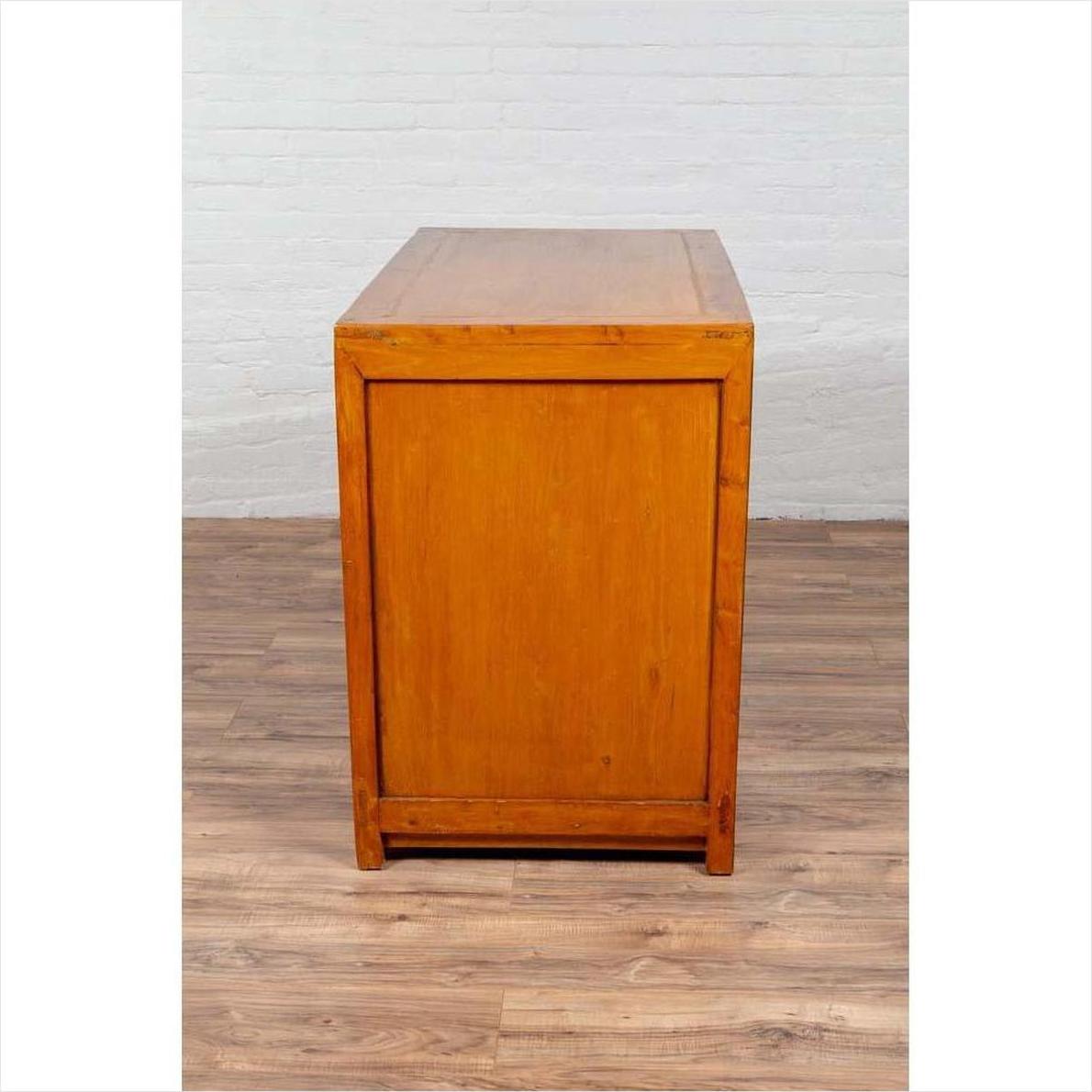 Two-toned burl and elm wood cabinet with doors, on a wooden floor next to a white brick wall.