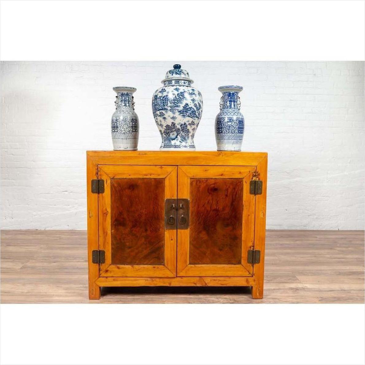 Two-toned burl and elm wood Chinese cabinet with doors, styled with blue and white vases on top, indoors.
