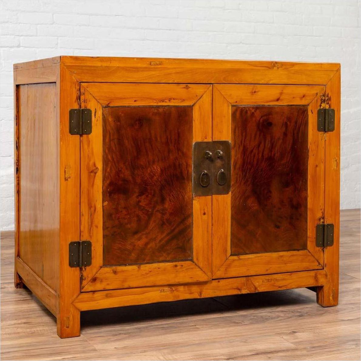 Two-toned burl and elm wood antique Chinese cabinet with doors, placed against a white brick wall indoors.