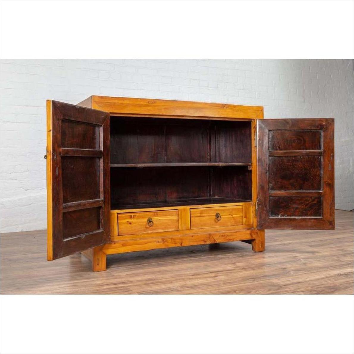 Two-toned burl and elm wood cabinet with doors, antique finish, positioned against a white brick wall indoors.