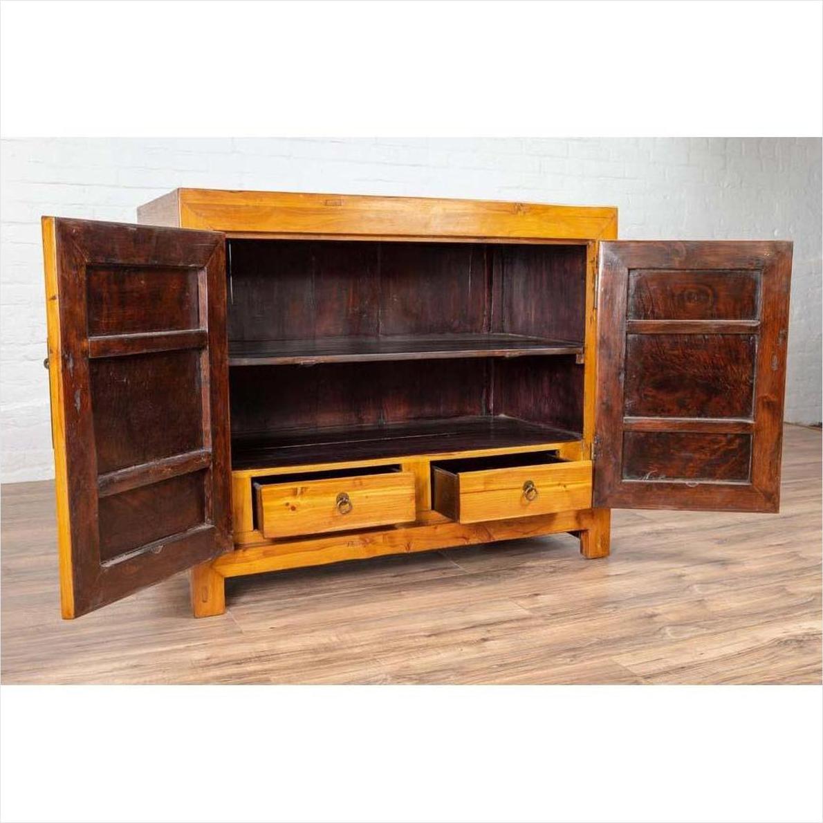 Brown burl and elm wood patina cabinet with doors, shelf, and drawers against a white wall on wood floor indoors.