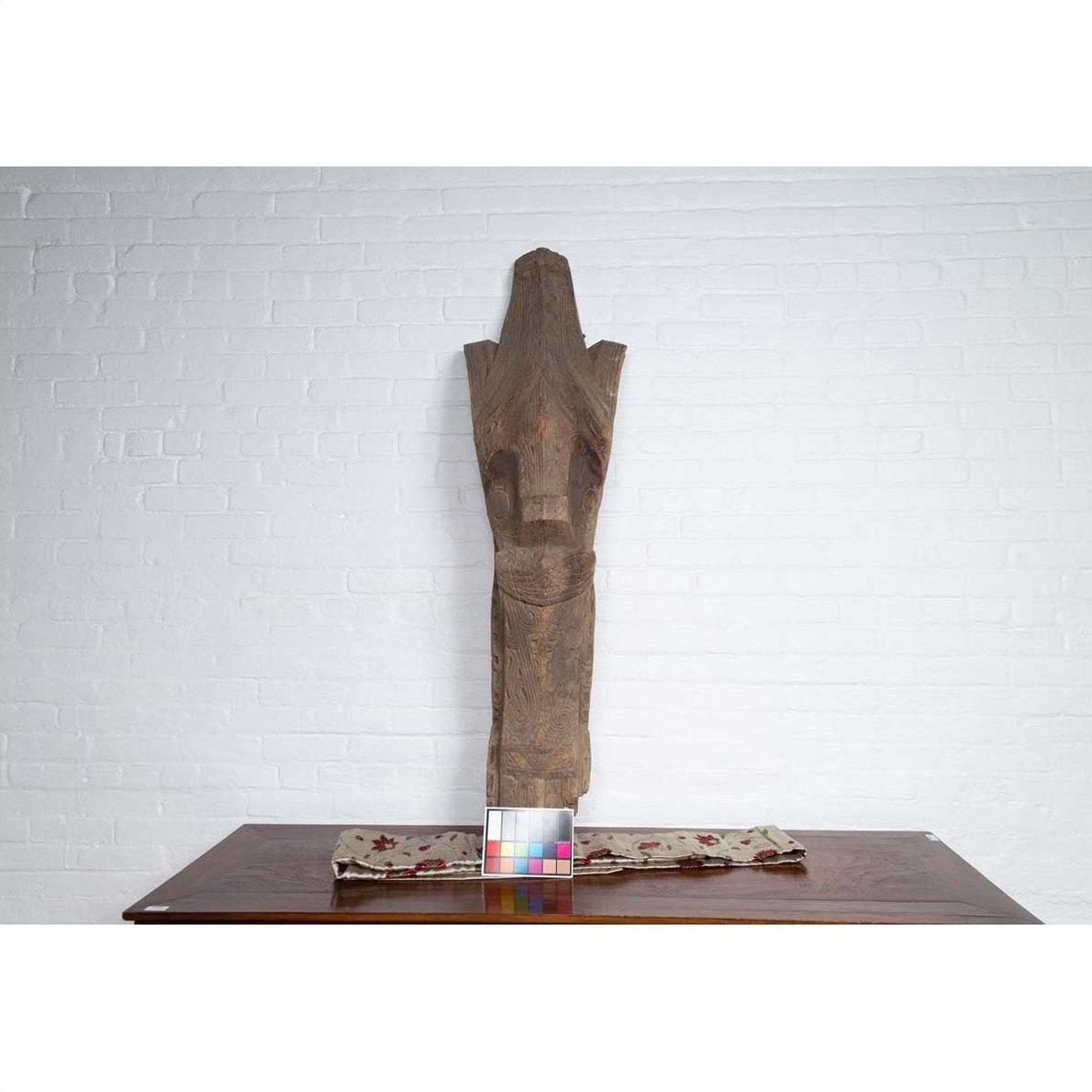 Brown wood Singa Singa Batak tribal carving on table against a white brick wall.