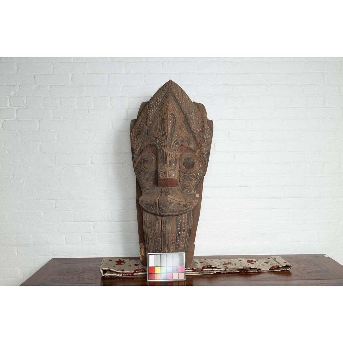 Brown hand-carved wooden Singa Singa tribal carving with patterned details from Batak people on table, chart in front.