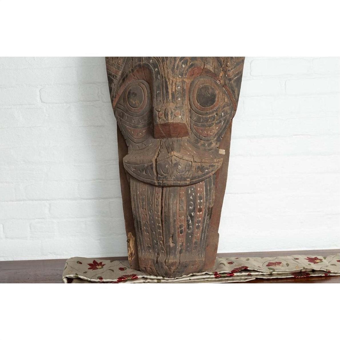 Brown hand-carved wood Singa Singa tribal figure from Batak people, Sumatra, on table with cloth.