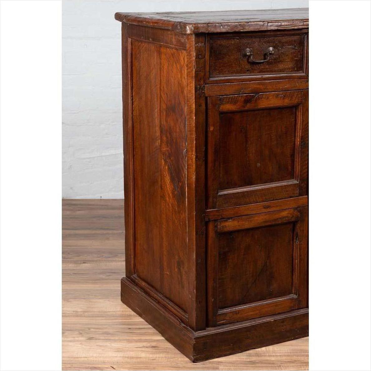 Brown teak wood cabinet with four drawers and four double doors, antique style storage furniture, indoor setting.