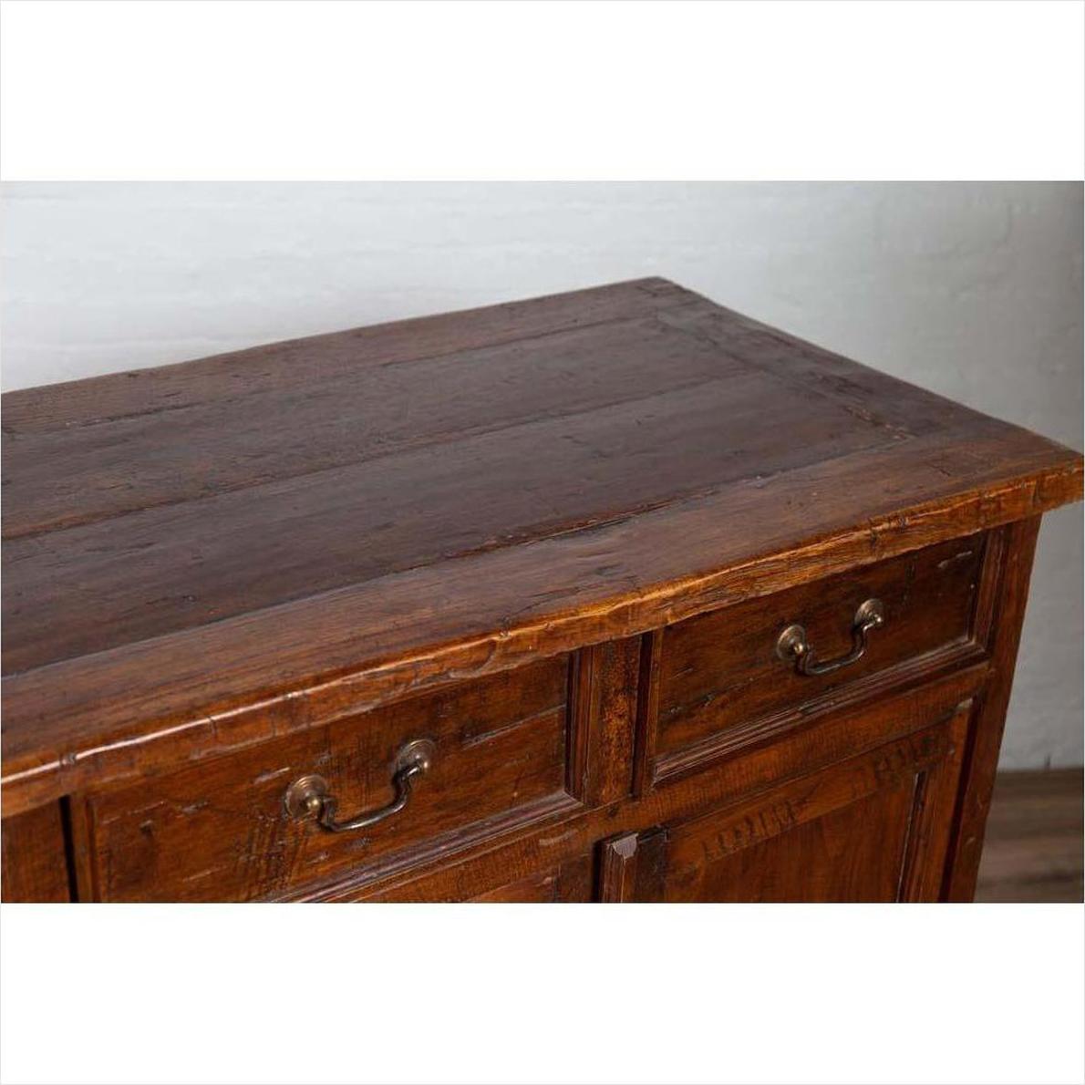 Close-up of brown teak wood cabinet with four drawers, double doors, and metal handles, indoors against a white wall.