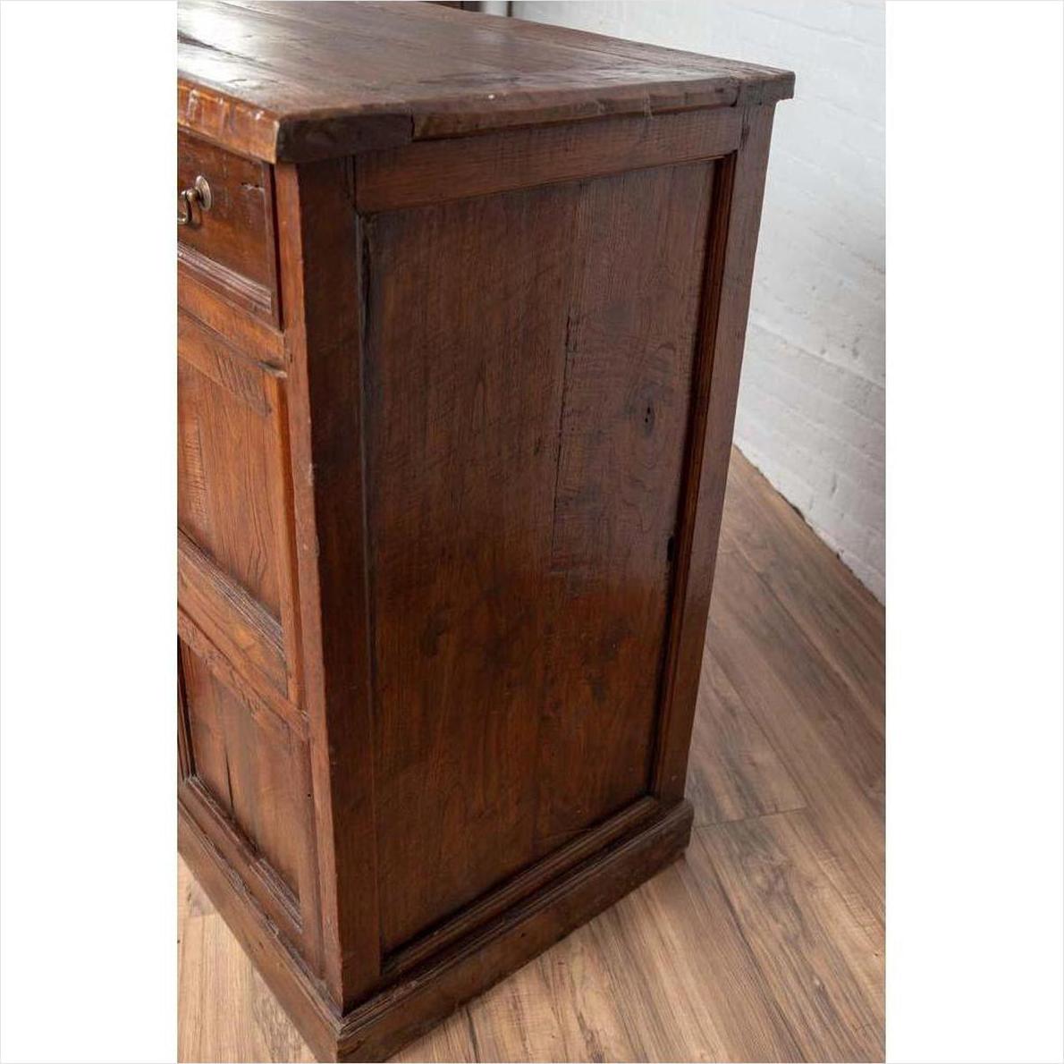 Close-up of a brown teak wood cabinet with four drawers and double doors on a wooden floor.