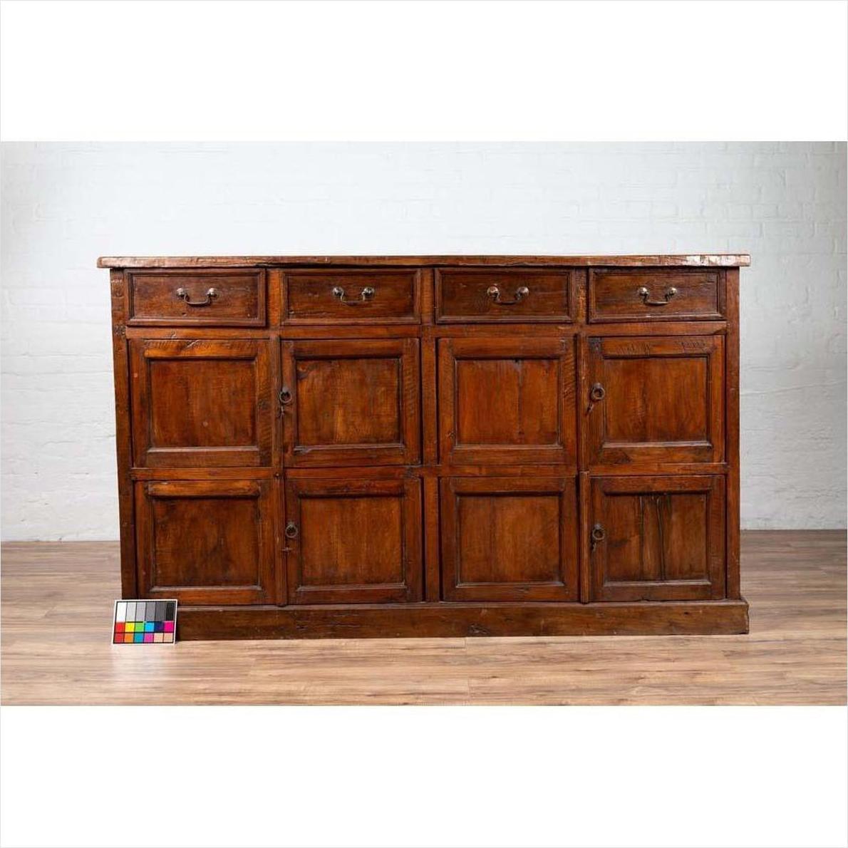Brown teak wood cabinet with four drawers and four double doors on a wooden floor indoors.