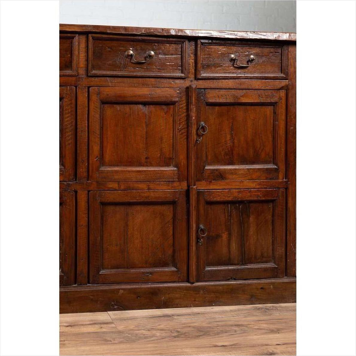 Close-up of a brown teak wood cabinet with four drawers and four sets of double doors, indoors.