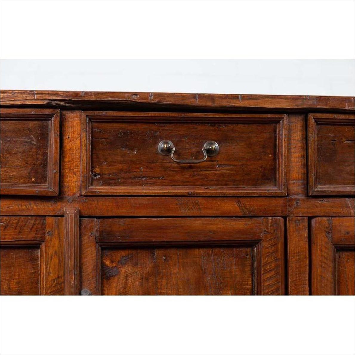 Close-up of brown teak wood cabinet drawer with metal handle; shows four drawers and double doors.