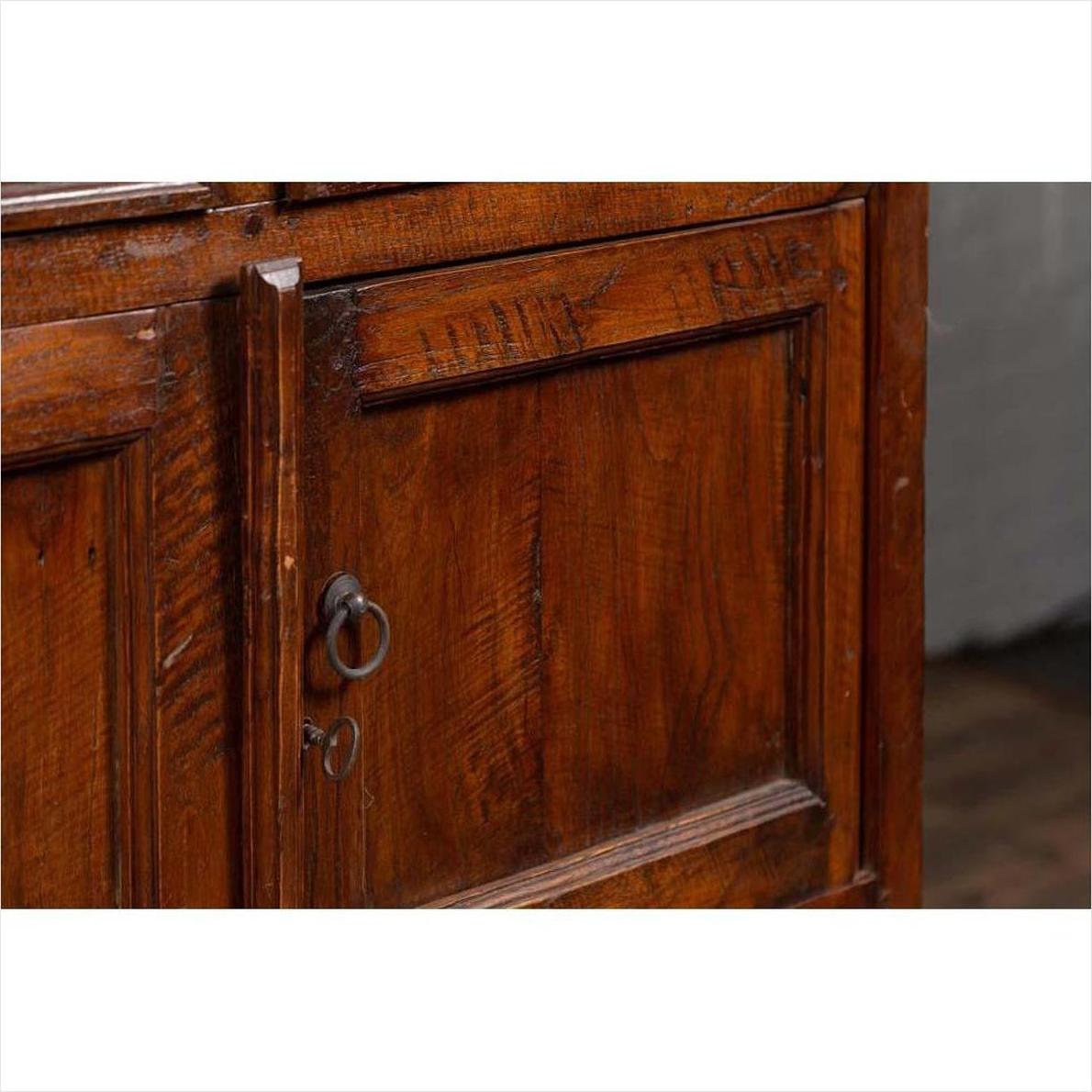 Close-up of brown teak wood cabinet door with metal keyhole, ring handle, double doors, and four drawers.