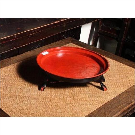Red round shallow tray with black legs, placed on a woven mat on a wooden table.