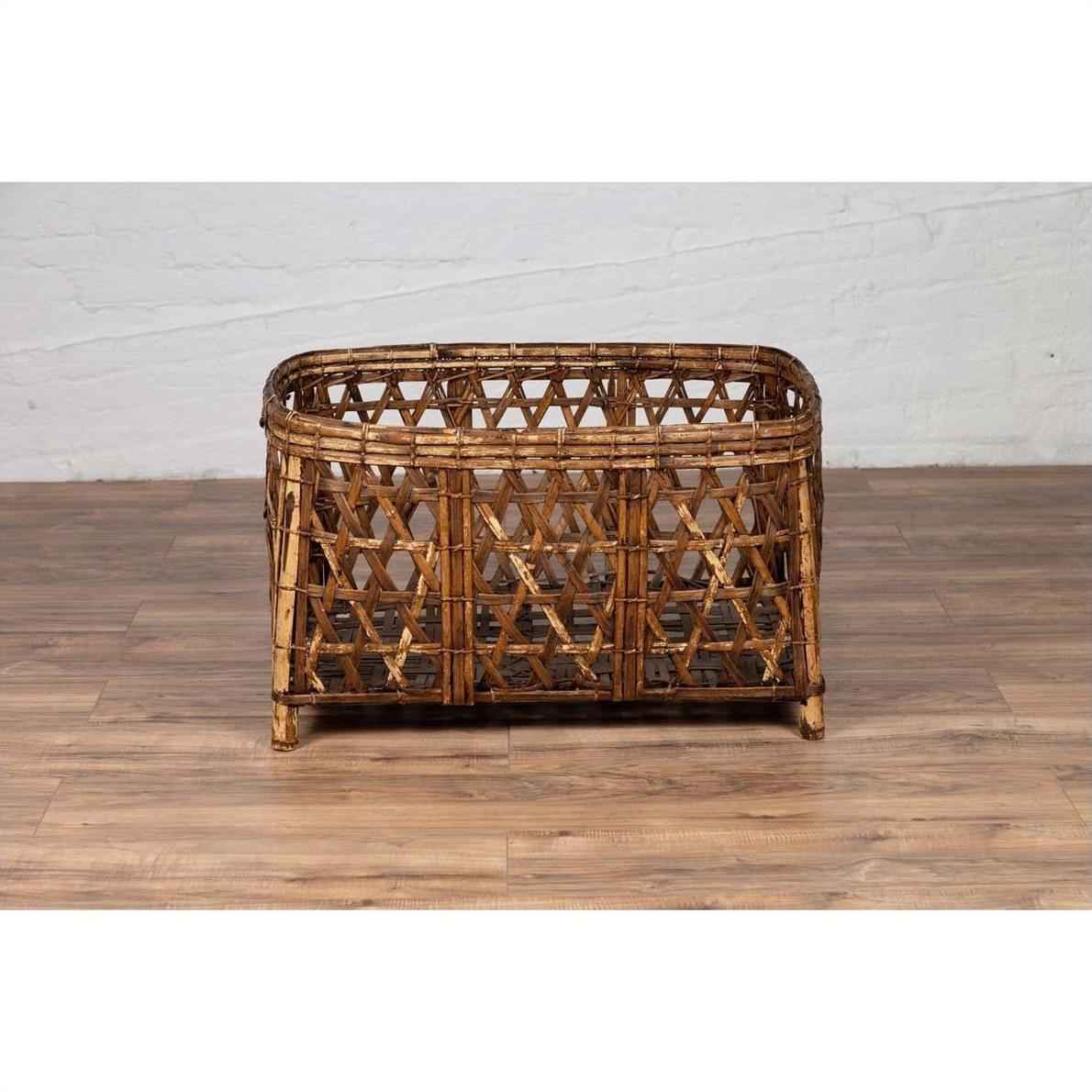 Vintage light brown bamboo fretwork basket with short feet on wooden floor against white brick wall, side view.
