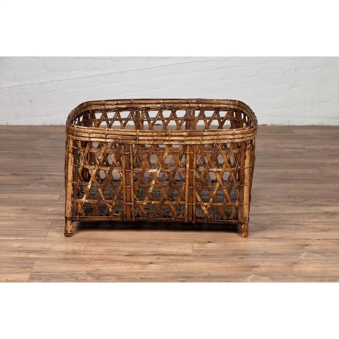 Brown bamboo fretwork basket with short feet, vintage Thai style, on wooden floor next to white brick wall.