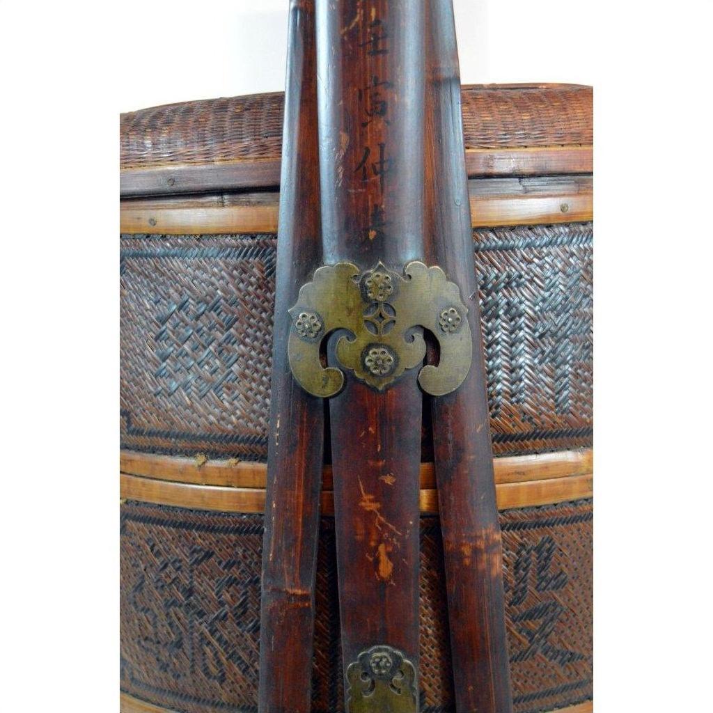 Brown carved wooden staffs with metal fittings resting against a large wicker basket with lid, indoor setting.