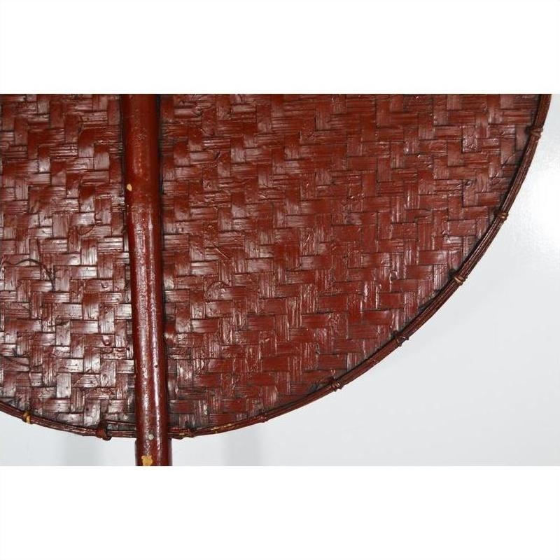 Close-up of a round brown woven fan with central handle, made from natural material, on a white background.