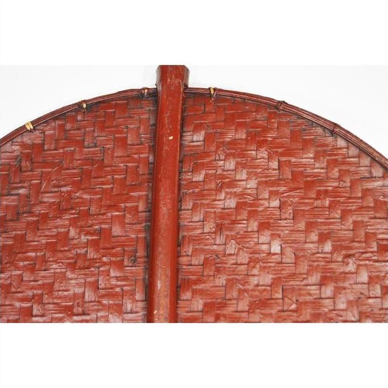 Close-up of a red-brown woven fan with circular design, wooden central handle, and intricate detailing.