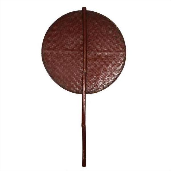 Close-up of a round, reddish-brown woven fan with a long handle, made from natural fibers.