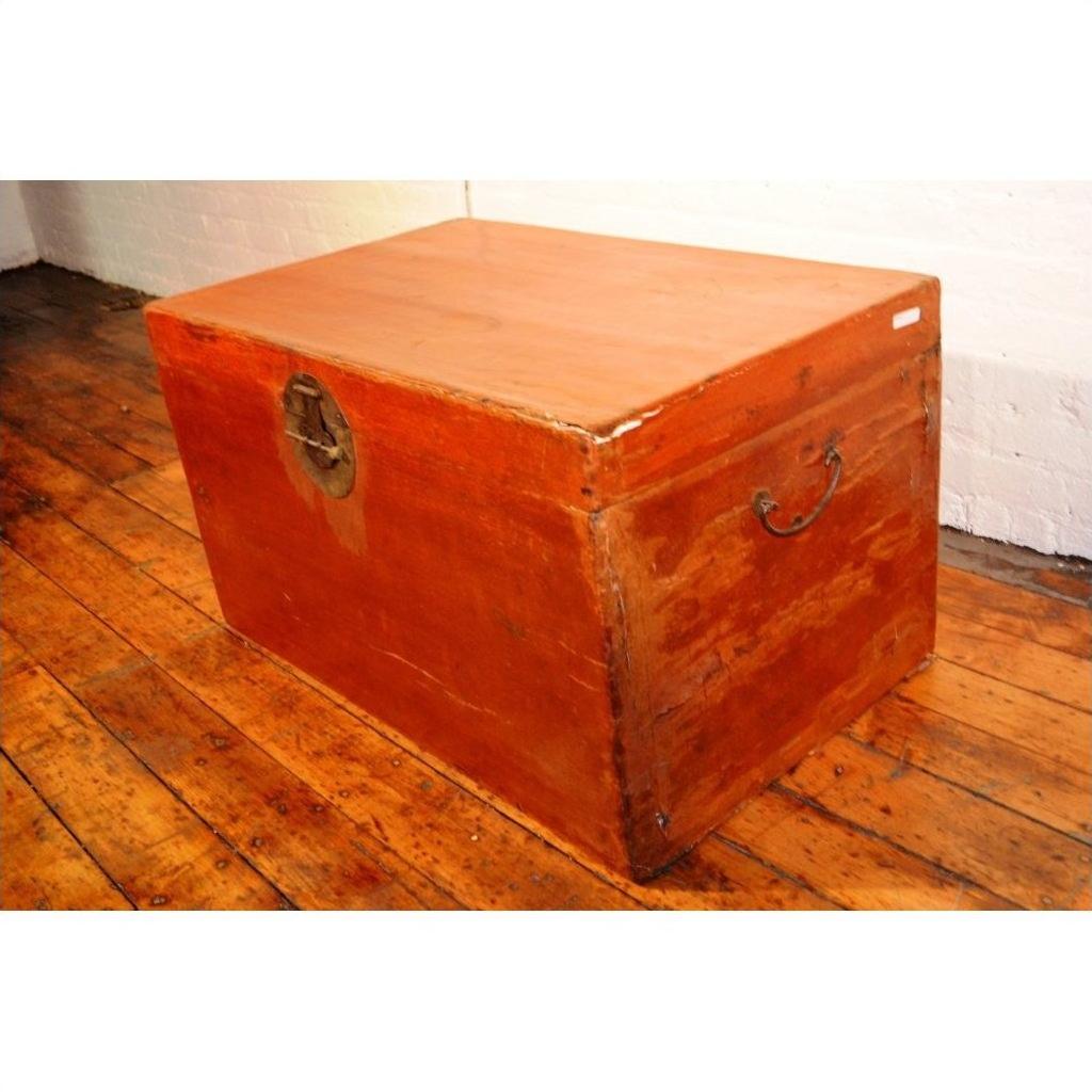 Brown leather coffee table trunk with metal handles on wooden floor beside a white brick wall.