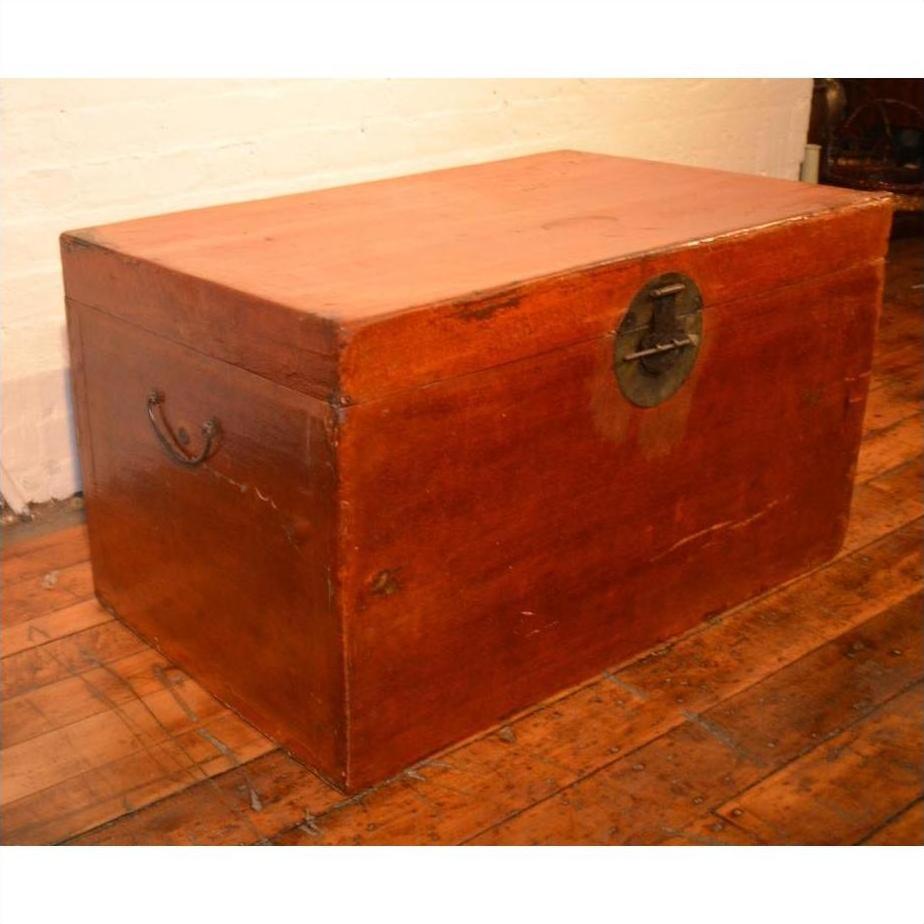 Brown leather coffee table trunk with metal handles and a round lock on a wooden floor by a white brick wall.