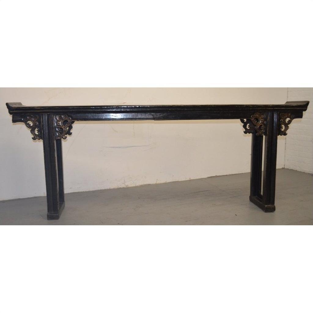 Long antique Chinese altar table with carved spandrels, dark wood, against a white wall and gray floor.
