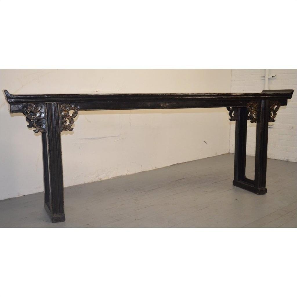 Black antique Chinese wood altar table with carved spandrels, positioned against a white wall and gray floor.