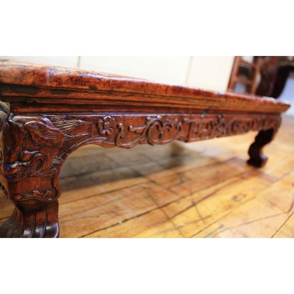 Close-up of a dark wood carved table with ornate floral designs and claw feet on a polished wooden floor.