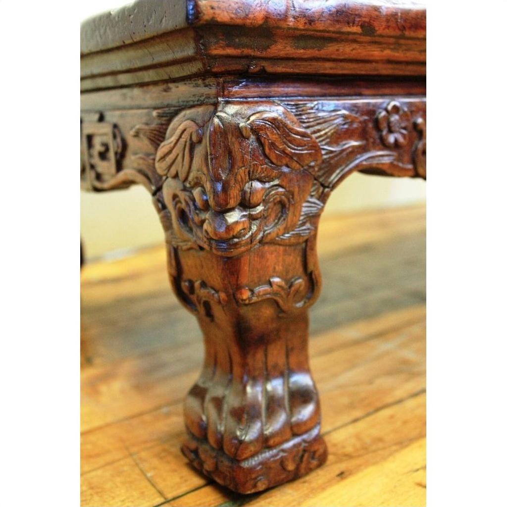 Brown carved wood table with floral and leaf motifs, claw feet, on polished hardwood floor.