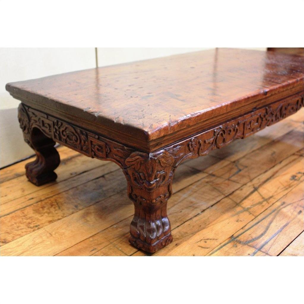 Brown wood low carved table with ornate carved legs and claw feet on a wooden floor.