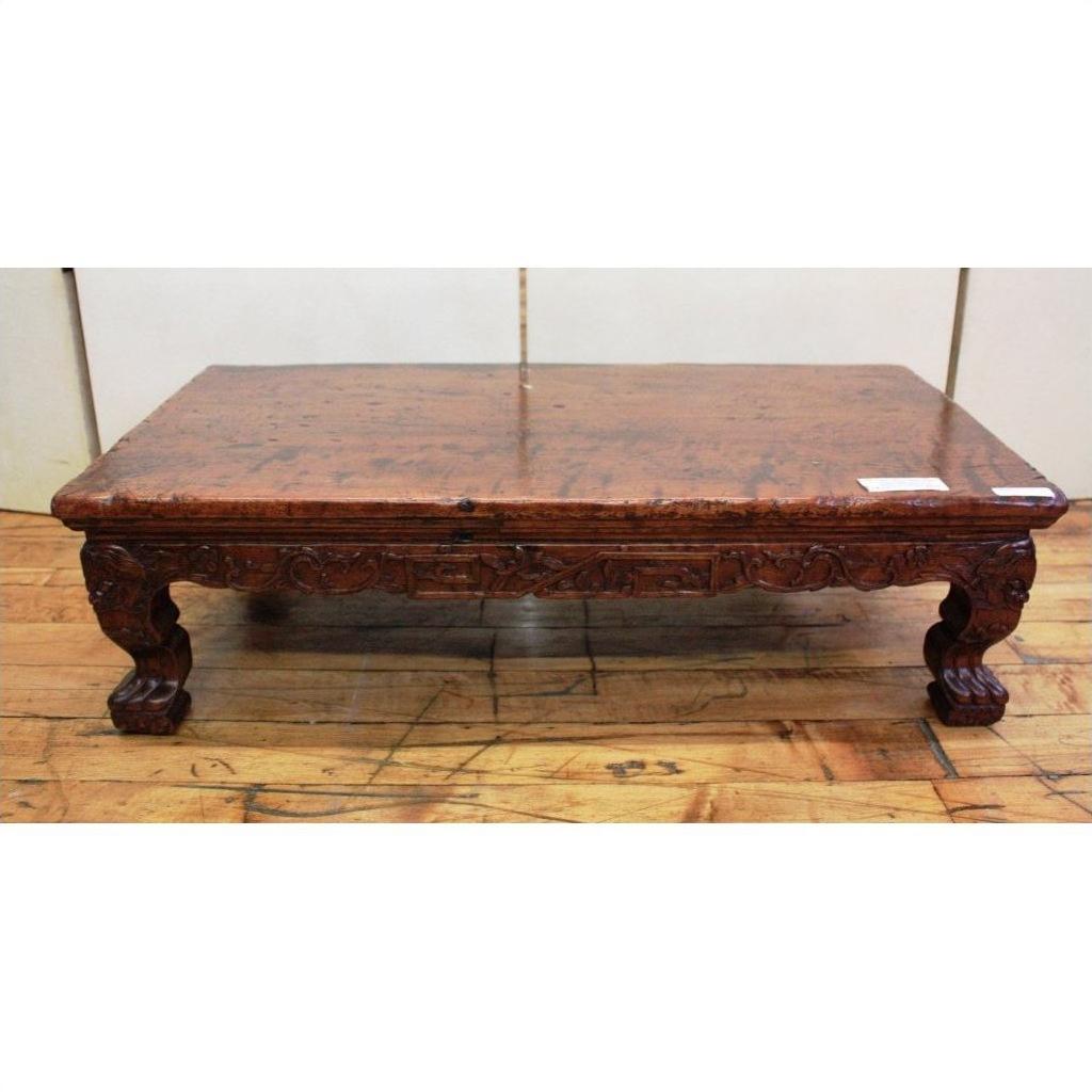 Dark wood low carved table with ornate legs and claw feet, placed on a wooden floor.
