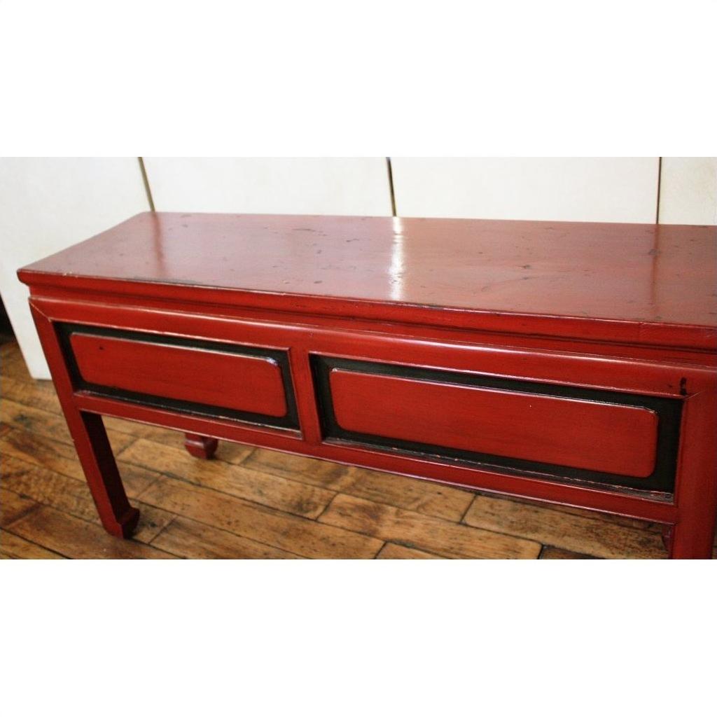 Red lacquer wood low side table with two black-trimmed rectangular panels on a wooden floor, light background.