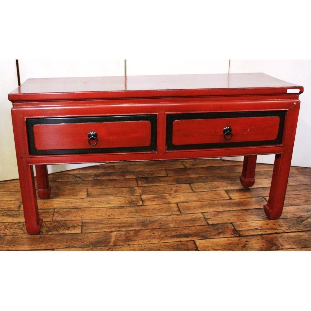 Red lacquer wooden side table with two black-trimmed drawers and ring handles on a wooden floor.