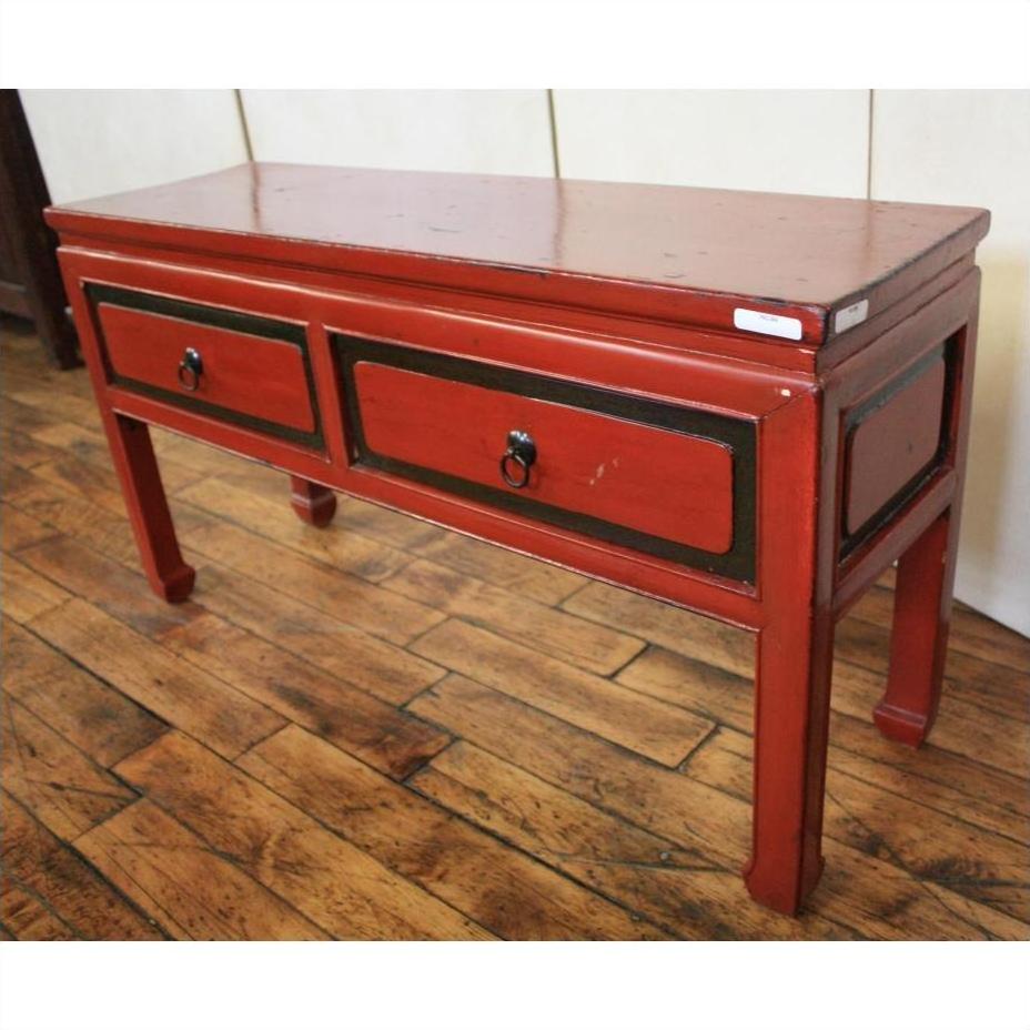 Red lacquer and black trim side table with two drawers on wood floor against a light-colored wall.