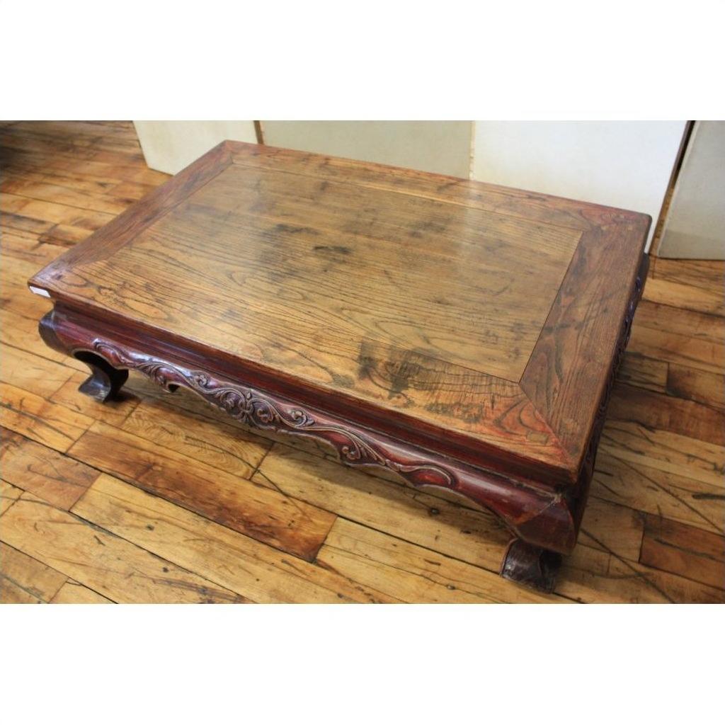 Square elmwood table with carved legs and ornate border on a hardwood floor, close-up view.