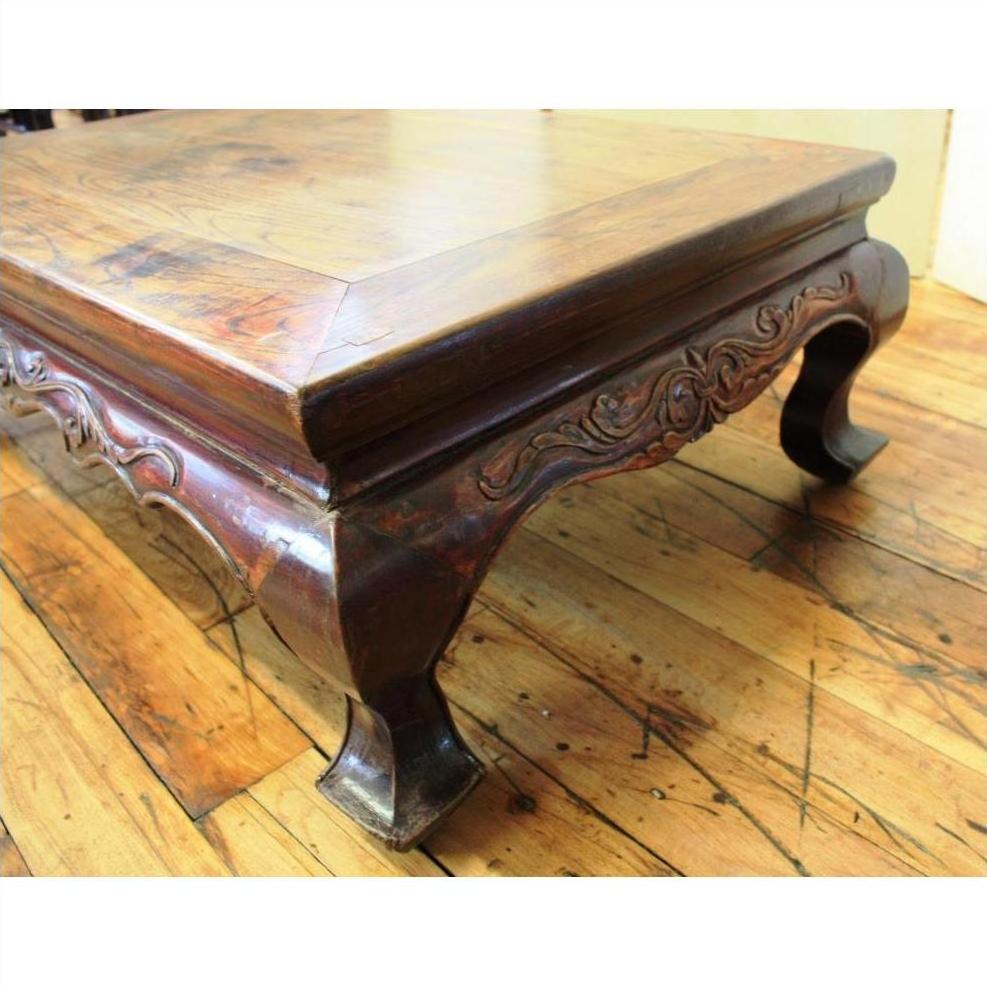 Brown wood square table with carved legs and decorative trim on a hardwood floor.