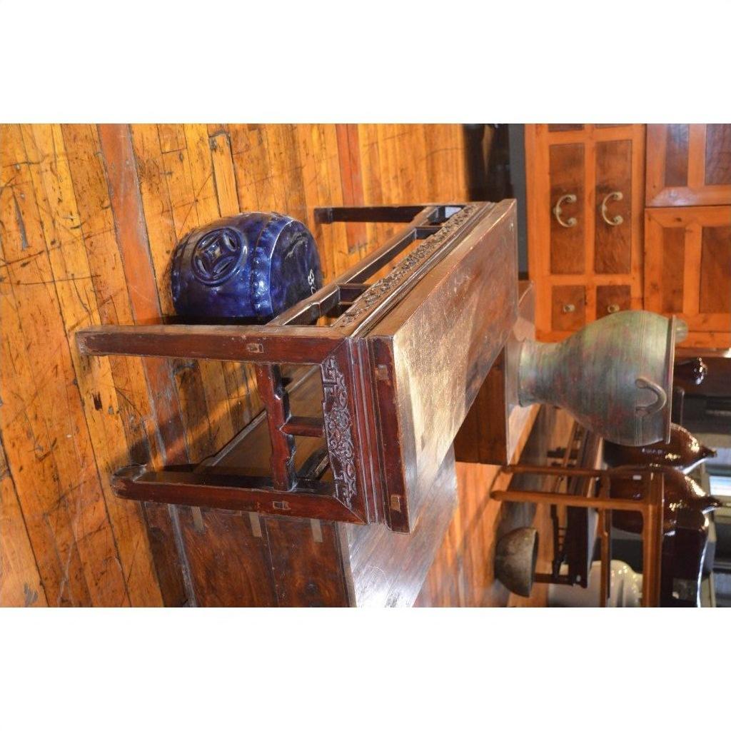 Wood low table with carved detail, blue ceramic piece, and green vase on polished wood floor, cabinets behind.