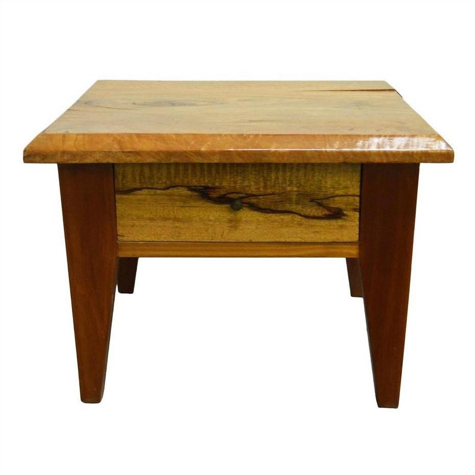 Natural mango wood side table with four legs, front drawer, and brass pull, shown in a close-up view.