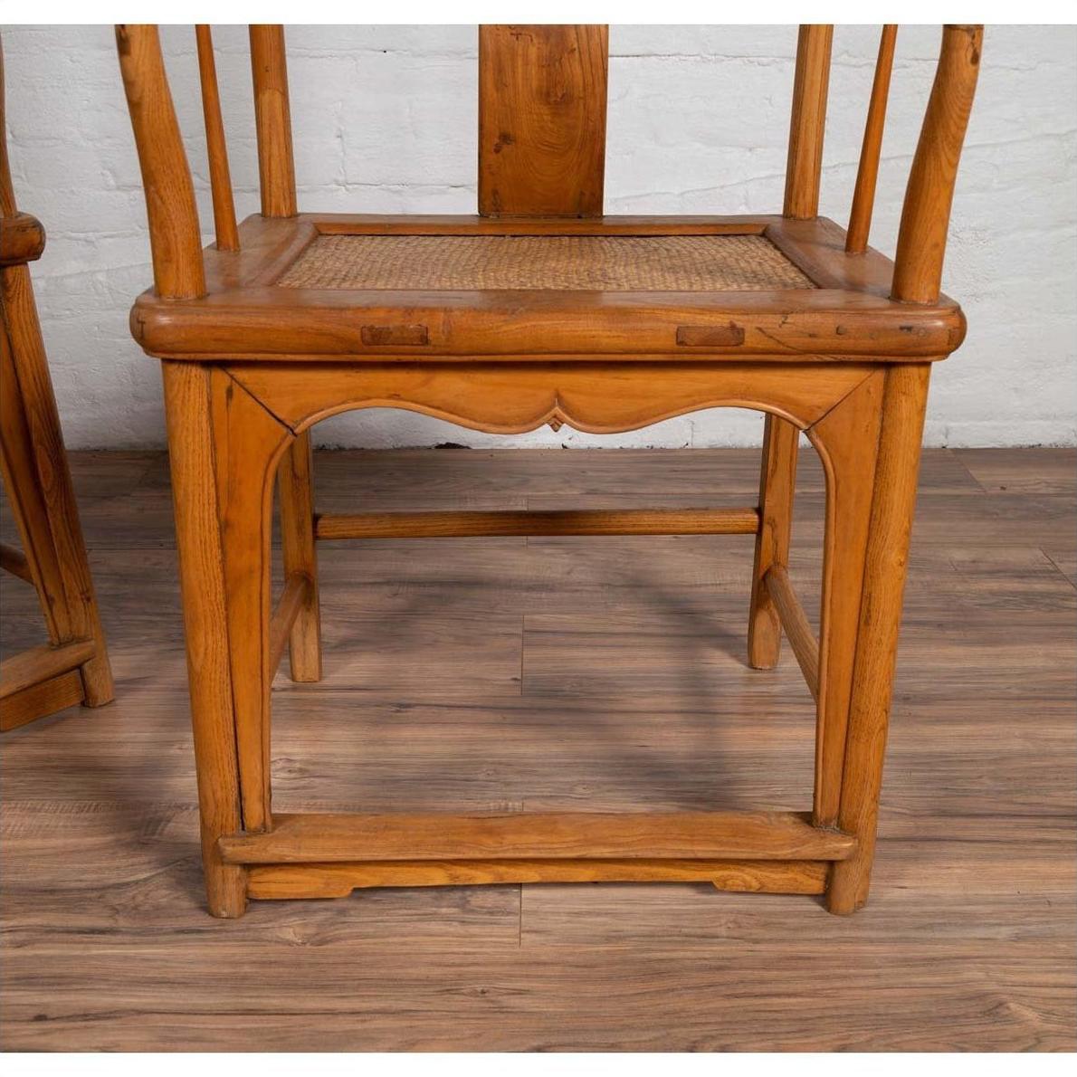 Brown wood and rattan Ming Dynasty style wedding armchair with curving arms on light brown floor by white brick wall.