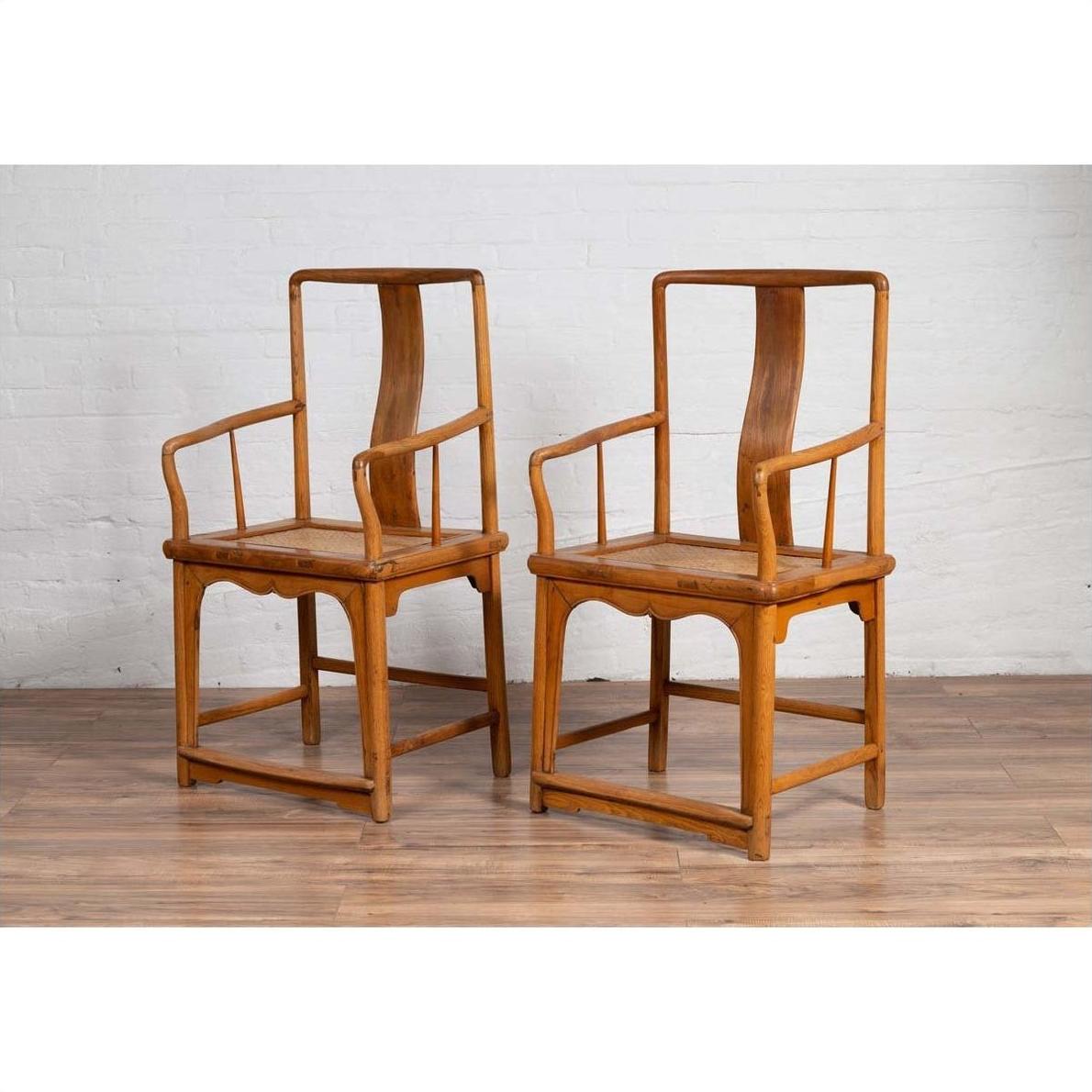 Brown wood and rattan armchairs with curved arms on a wooden floor against a white brick wall indoors.