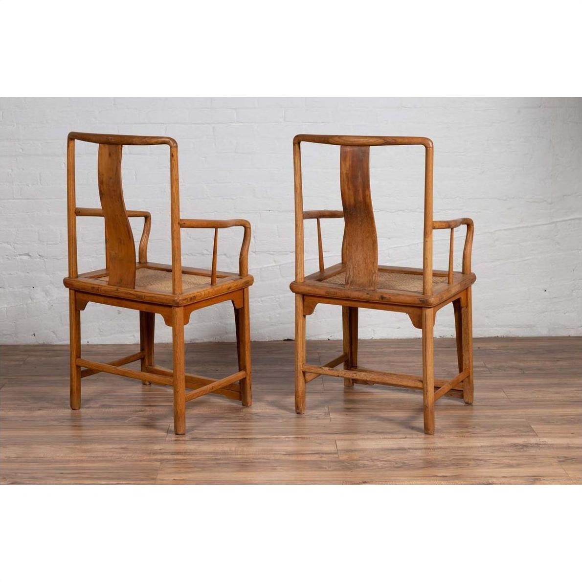 Brown wood and rattan armchairs with curved arms, pair set on wooden floor against a white brick wall indoors.