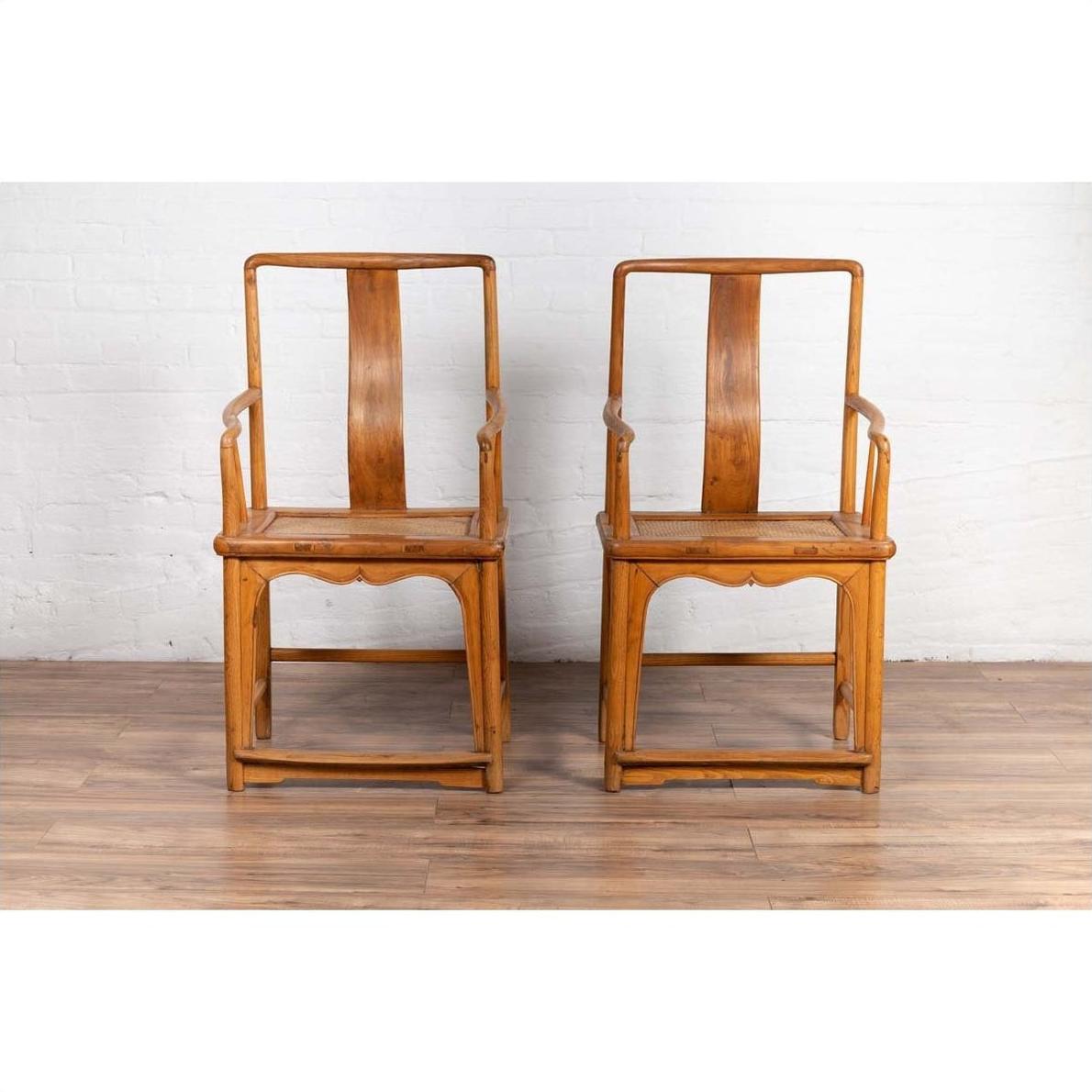 Brown wood and rattan Ming Dynasty style armchairs with curved arms, side by side on wooden floor indoors.