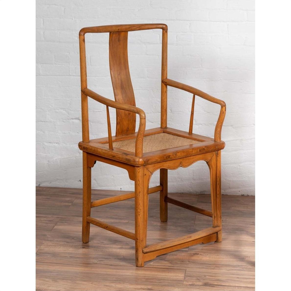 Brown wood and rattan armchair with curved arms, placed indoors against a white brick wall.