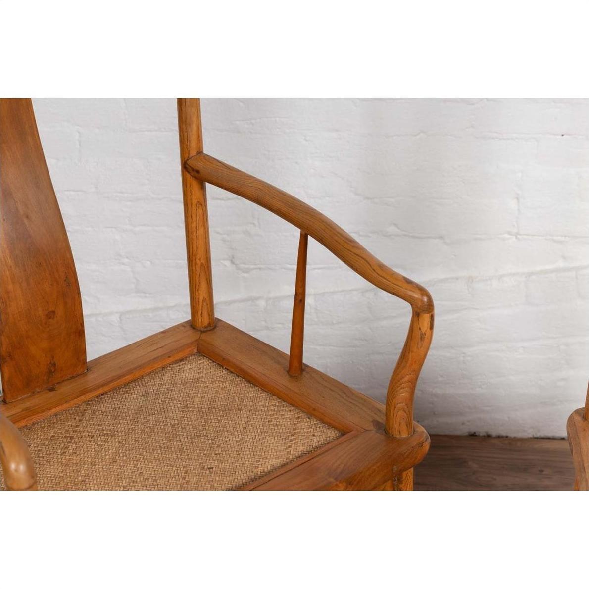 Close-up of brown wooden Ming Dynasty style wedding armchair with curved arms and rattan seat indoors.